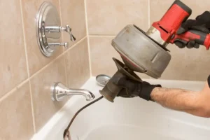 %Focuskw% | Get Lit Electrical, Plumbing &Amp; Hvac A person uses a power drain snake to clear a clogged bathtub drain in a tiled bathroom.