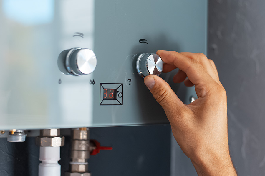 A hand adjusts the temperature knob on a wall-mounted water heater, with a digital display showing the temperature in Celsius.