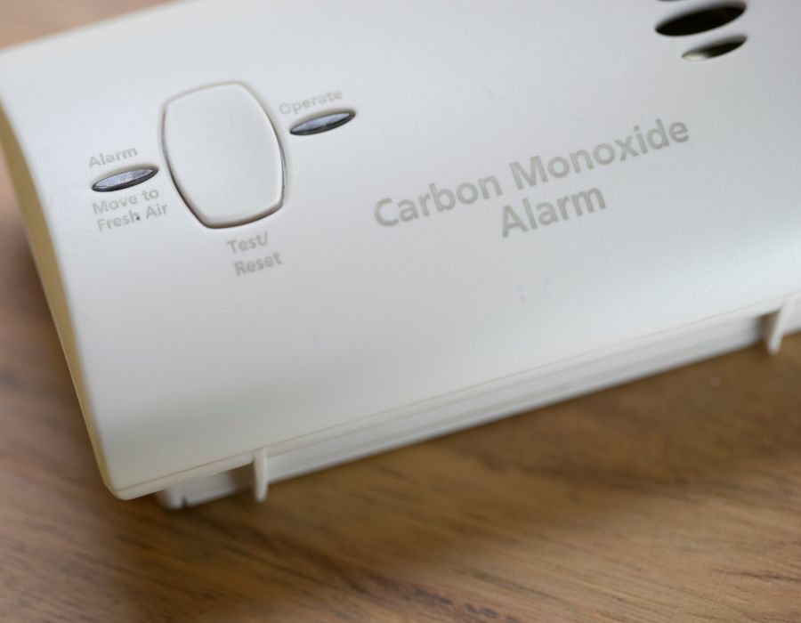 Close-up of a white carbon monoxide alarm on a wooden surface, showing the test/reset button and labeled instructions.
