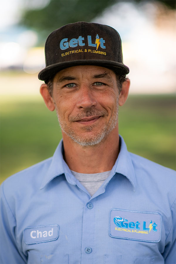 A man wearing a "Get Lit Electrical & Plumbing" hat and shirt with the name tag "Chad" stands outdoors, looking at the camera.