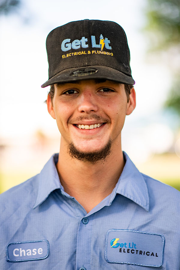 A young man wearing a "Get Lit Electrical & Plumbing" hat and shirt, with a name tag that says "Chase," smiles at the camera outdoors.