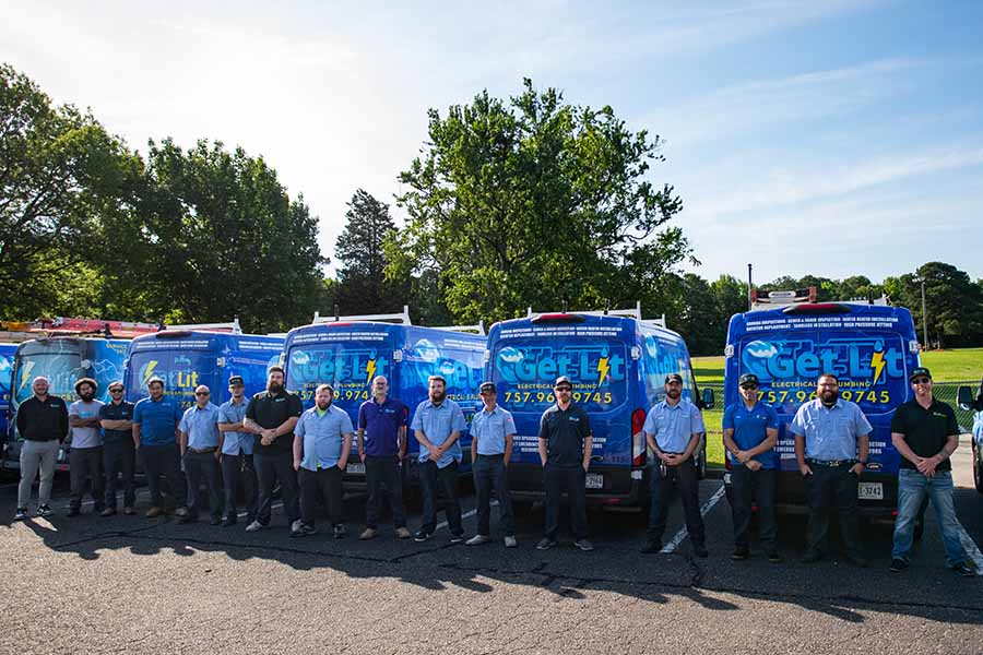 A group of people stands in front of a row of blue service vans with "Get Lit" and contact information printed on the back, highlighting careers and jobs available as the company is now hiring, in a parking lot with trees in the background.