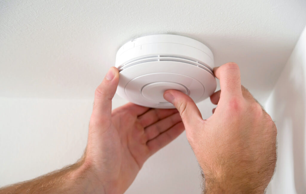 Hands attaching a white smoke detector to a ceiling.