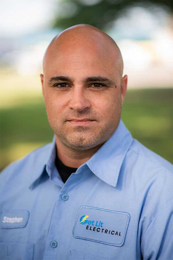 A man in a light blue work shirt with "Get Lit Electrical" logo and a "Stephen" name tag, standing outdoors with a blurred background.