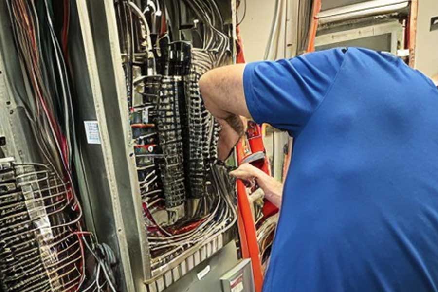 Person in a blue shirt working on electrical wiring inside a panel, using tools to adjust components.