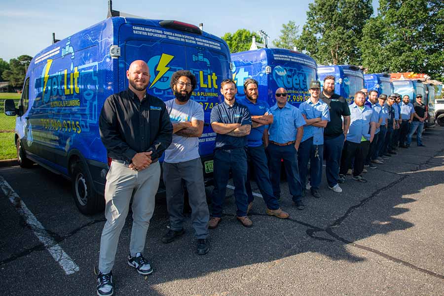 A group of uniformed workers stands in a line beside several blue service vans in a parking lot on a sunny day, ready to serve—discover more about us and our dedicated team.